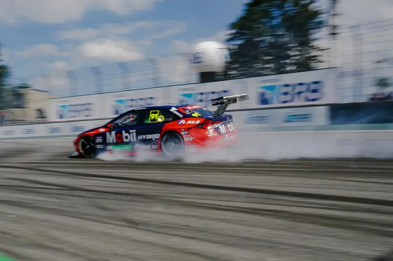 Race car spinning its wheels in front of grandstand banners