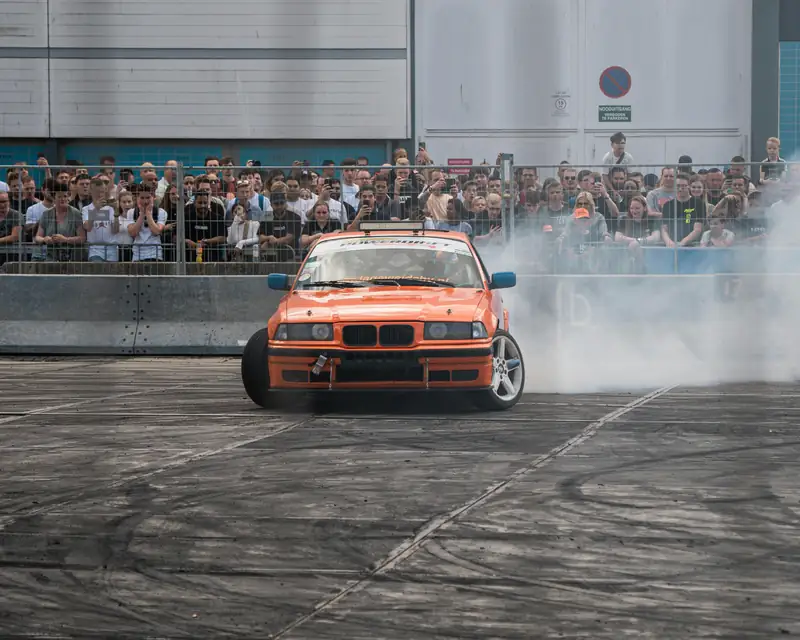 Orange BMW drifting in front of a crowd